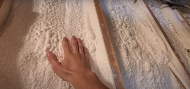 Spray foam insulation applied to a wall panel with a hand feeling its texture
