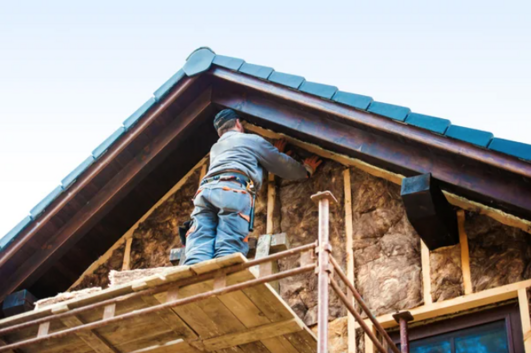 Worker standing on scaffold installing rock-wool batt insulation on the exterior of an attic